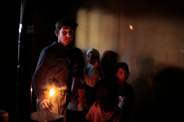 Ahmad, 13, and his siblings come to watch their mother be examined by volunteer Dr. Batley. He brings a candle to show the doctor the frostbite on his mothers feet that is badly infected. There house has no running water, electricity, or furniture. The woman rest on a small mat on the floor of a dark shelter that the family of ten occupied when they fled the fighting in Al Qusair, Syria. Photo by Omar Alkalouti.