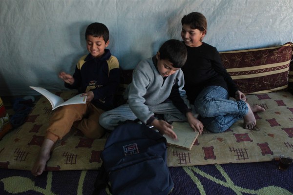 Faisal, 6, Hazim, 7, and Asmahan, 11, flip through Hazim’s books in their tented home in the Masaab Telyani camp Zahle, Lebanon.