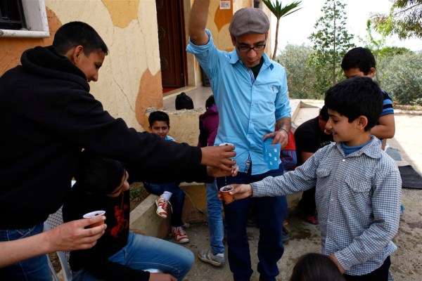 Firas Abi Ghanem, Intersos project coordinator in the Chouf, runs an activity where he is helping a new group of Syrian refugees learn how to let the water out of the bottom of their cups, which have freshly planted basil seeds.